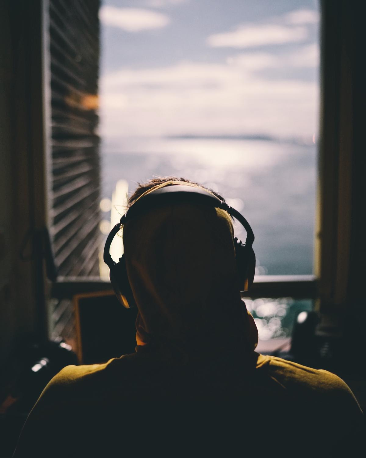 An image showing a person with headphones on, listening to a podcast while holding a smartphone. Visual depiction of the topic of podcast monetization.